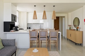 A modern kitchen with white cabinetry, a dining area with wooden chairs, and pendant lighting. - Vesta - Luxury APT - 1BR - Fairway (El Gouna)