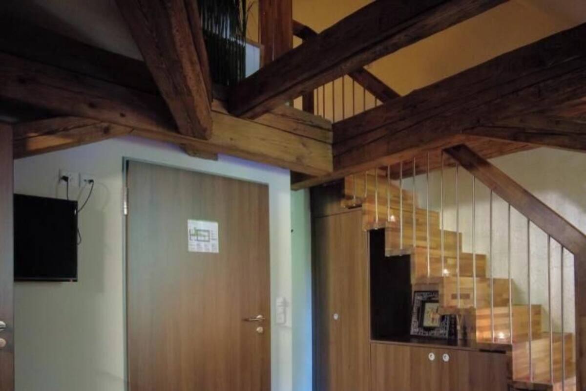 Une pièce avec un escalier en bois, une porte avec une pancarte et une petite table sur laquelle se trouve un cadre photo.