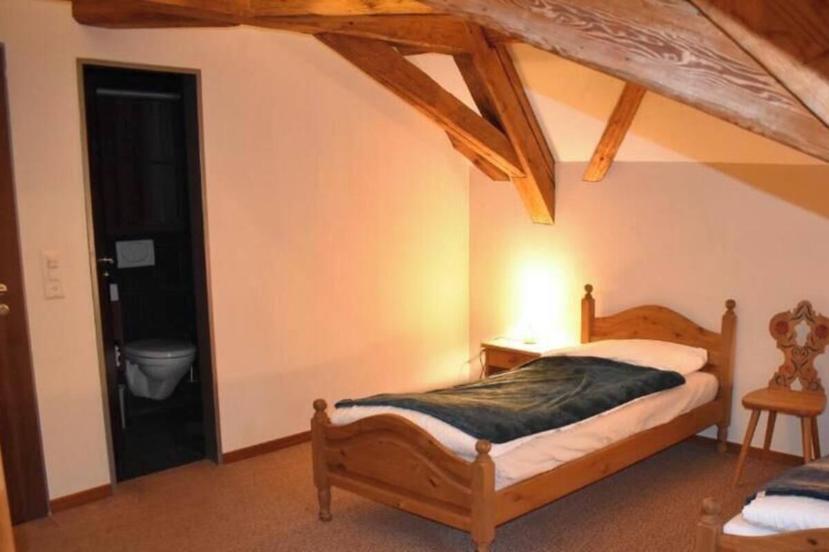 Une chambre avec un plafond en pente, des cadres de lit en bois, une table de chevet avec une lampe et une porte donnant sur une salle de bain.