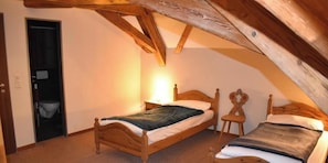 A bedroom with a sloped ceiling, wooden bed frames, a bedside table with a lamp, and a door leading to a bathroom. - Hotel Herberge (Teufenthal)