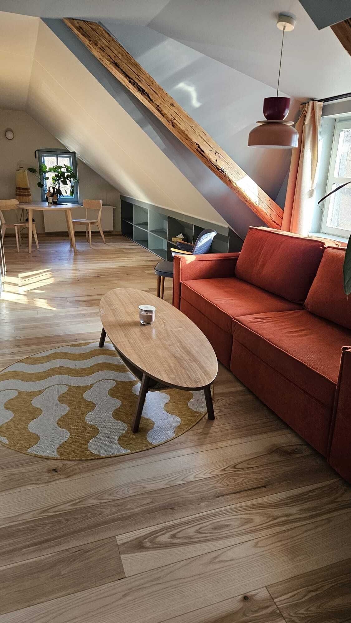 Un appartement moderne de style « loft », avec un plafond en pente, une table à manger en bois, un canapé rouge et un petit téléviseur en arrière-plan.