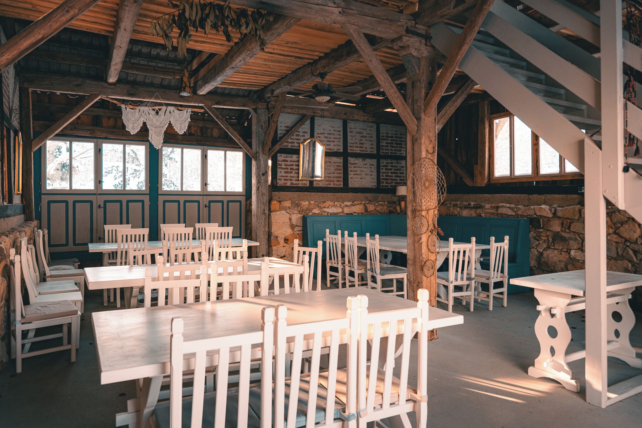 Un coin repas rustique avec des tables et des chaises en bois, des murs en pierre et une vue sur l’extérieur.