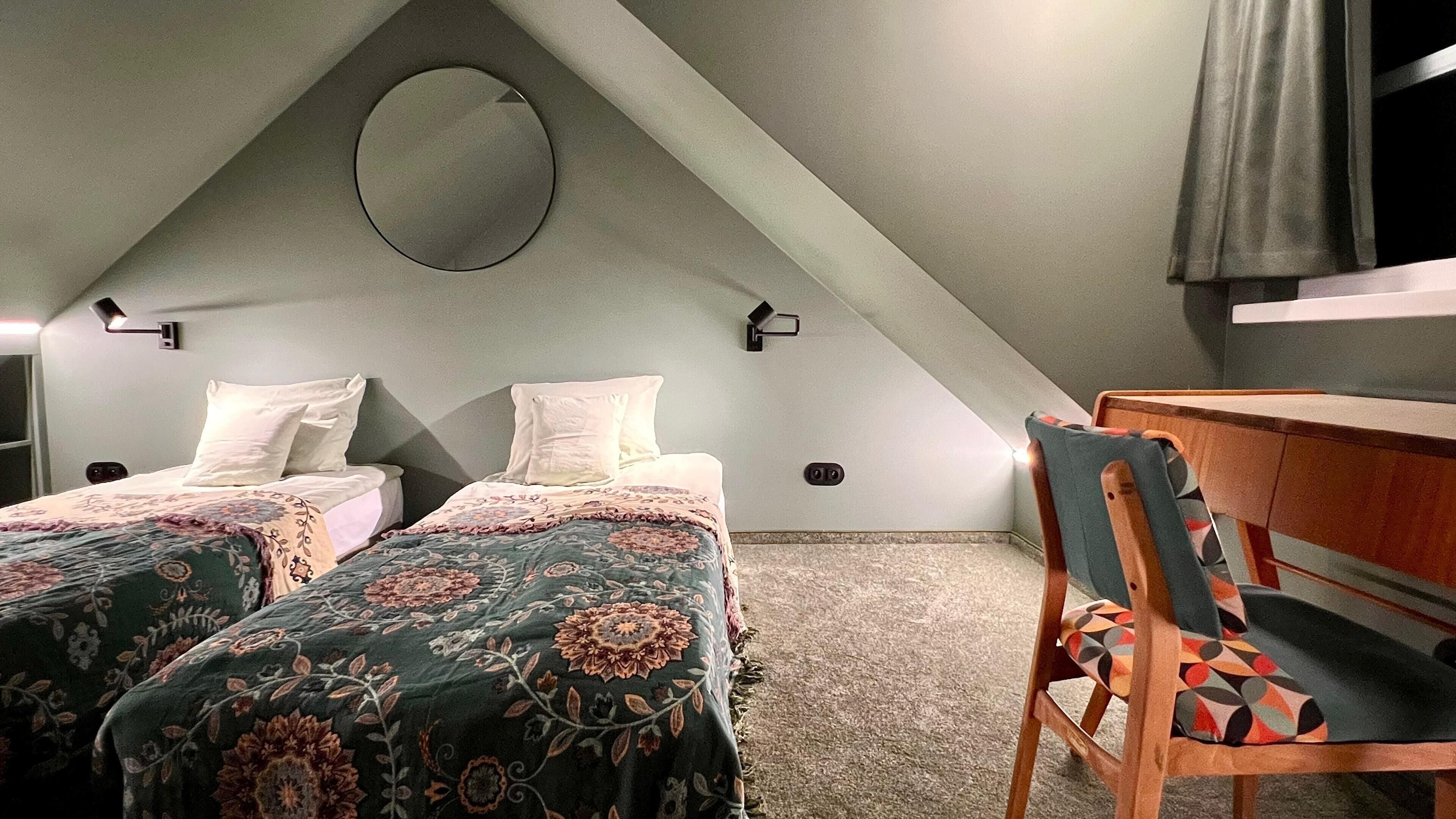 A small, cozy attic bedroom with two beds, a desk, and a chair.