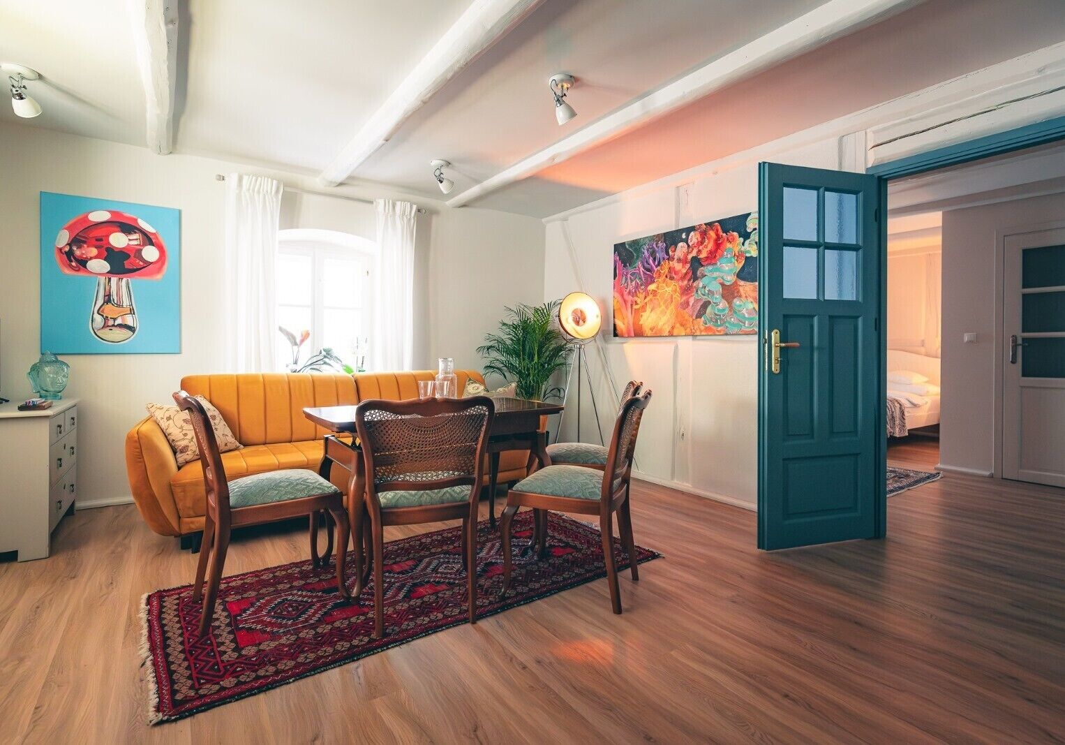 A living room with a sofa, dining table, chairs, a lamp, and a painting.