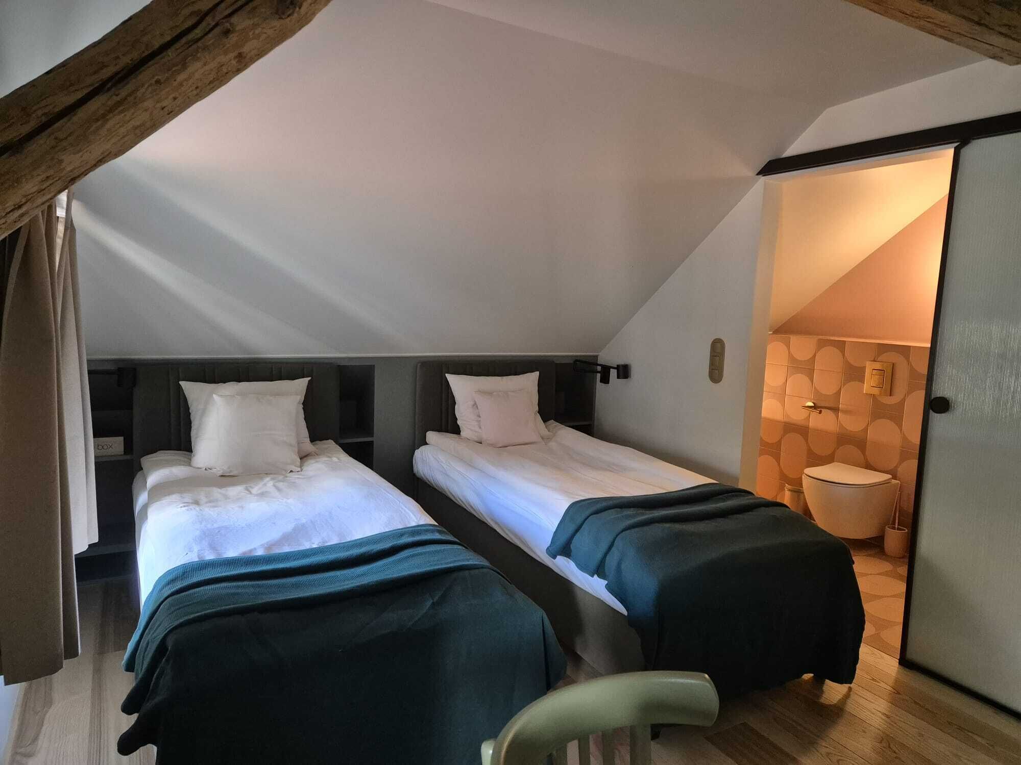 Een kamer met twee bedden, een houten plafond, een kleine stoel en een badkamer zichtbaar door een open deur.