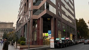 Un bâtiment moderne avec une entrée d’angle bien visible, de grandes fenêtres et un panneau indiquant la présence d’un parking.