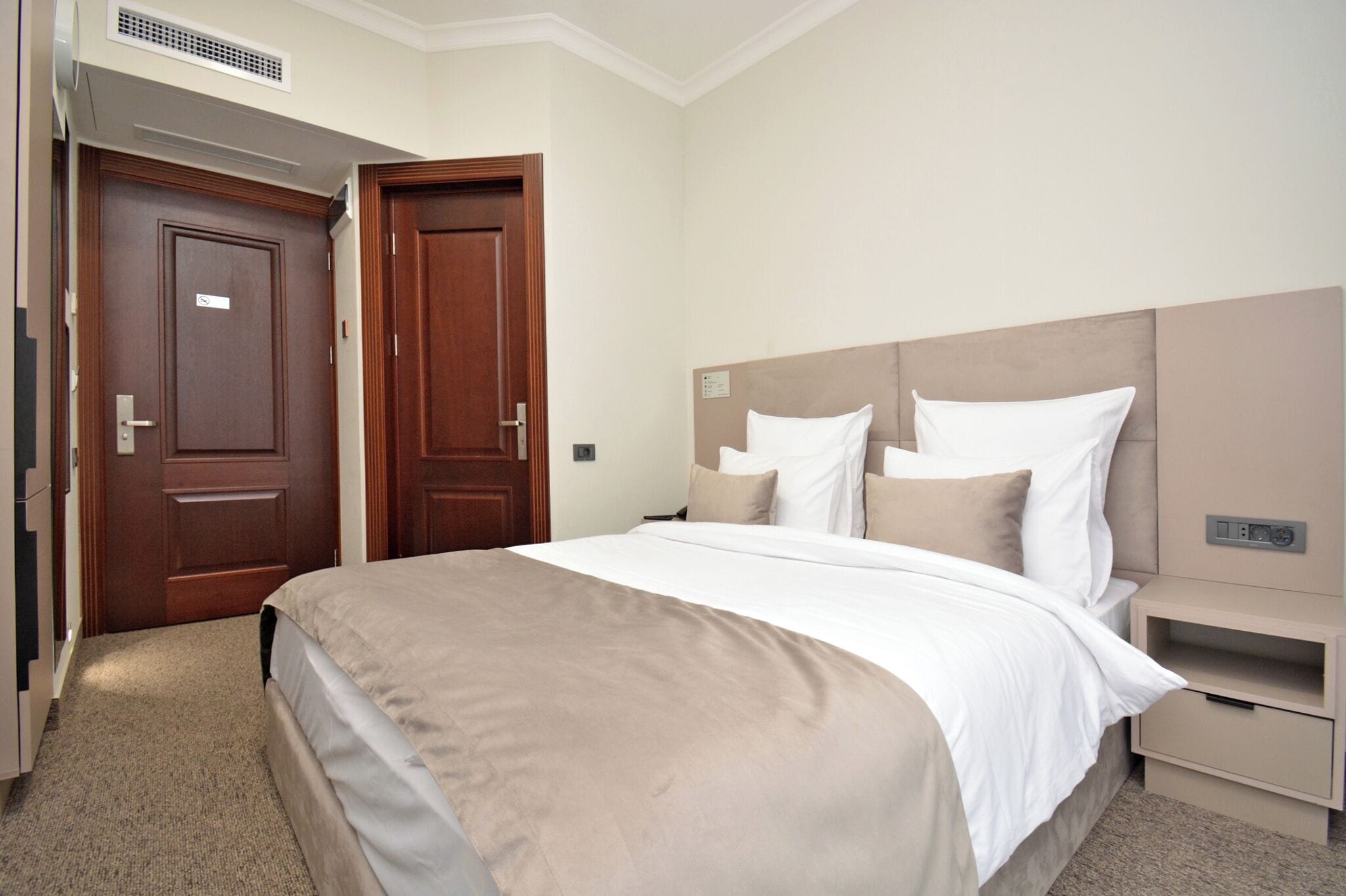 A hotel room with a large bed, a wooden door, and a nightstand with a lamp.