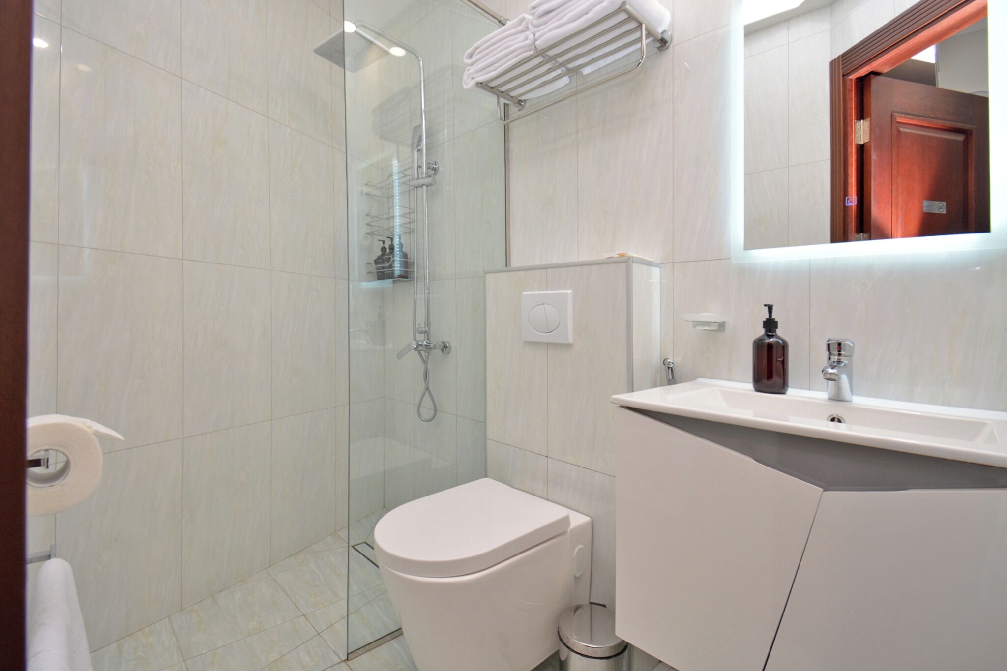 A modern bathroom with a glass-enclosed shower, a white toilet, and a sink with a mirror above it.