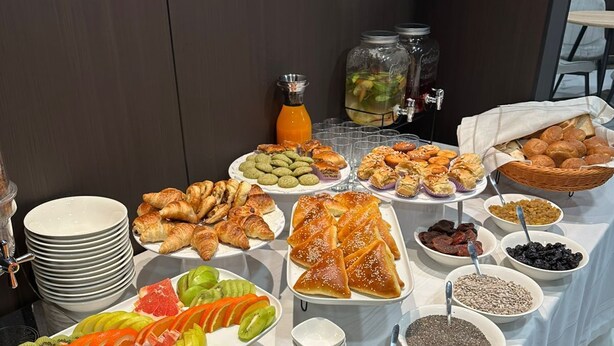 Une table de buffet proposant une variété d’aliments, notamment des pâtisseries, des fruits et des condiments.
