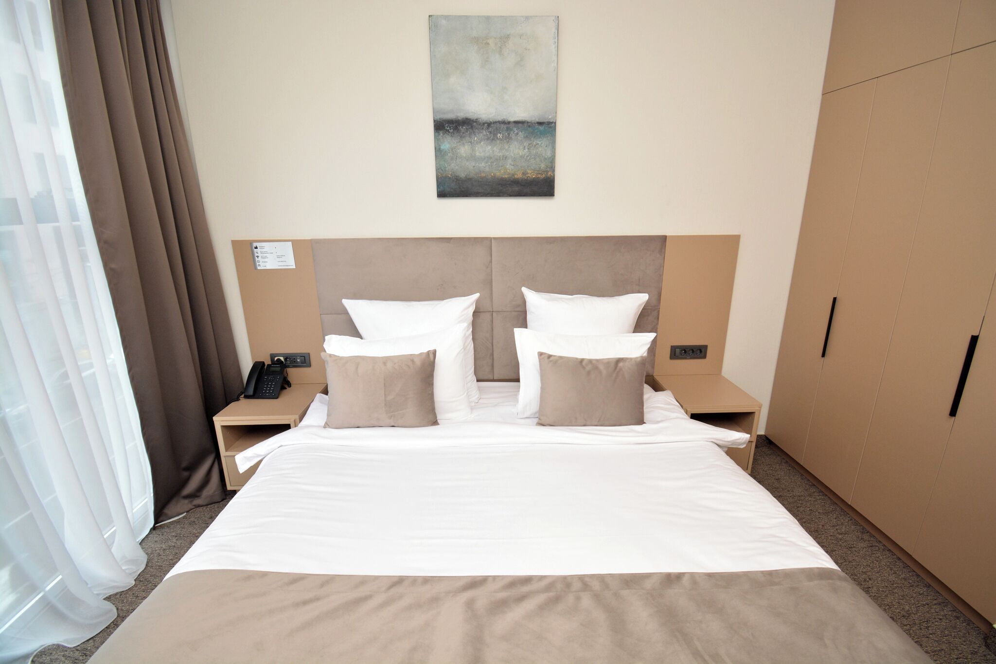A hotel room with a large bed, two bedside tables, a nightstand, a telephone, and a wardrobe.