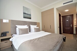 Een hotelkamer met een groot bed, een nachtkastje met telefoon, een schilderij aan de muur en een kledingkast.