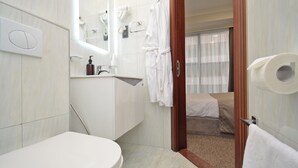 Une salle de bain moderne avec des toilettes, un lavabo et un miroir. Une robe est accrochée au mur et une serviette est posée sur le sol.