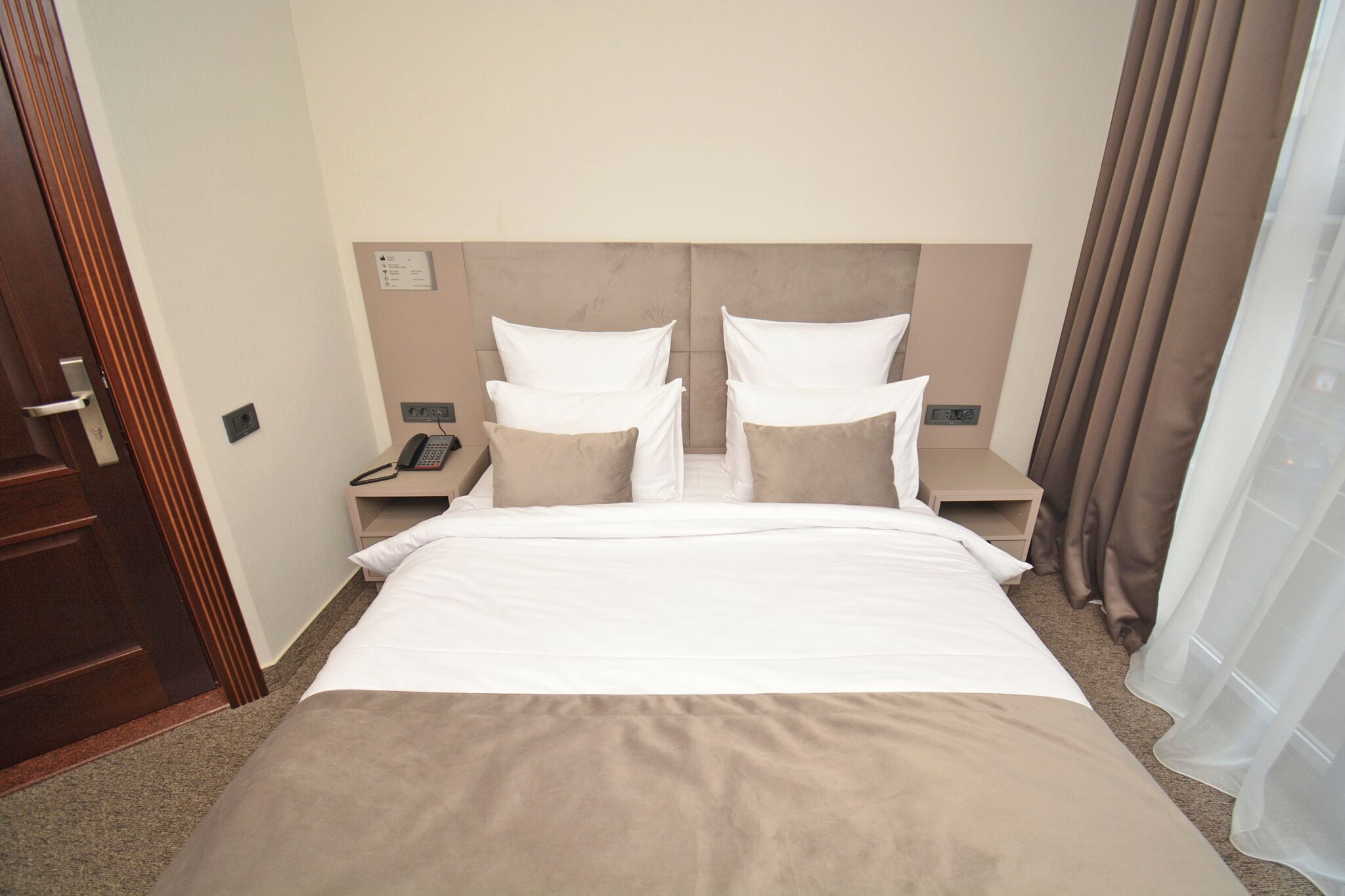Una habitación de hotel con una cama grande, dos mesitas de noche, un teléfono y un panel de control en la pared.