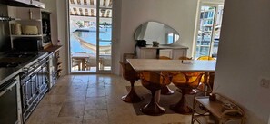 A kitchen with a stove, oven, and cabinets, a dining area with a table and chairs, and a view of a water body and buildings through a glass door.