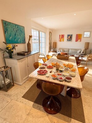 A dining area with a long table set for a meal, a kitchen area with a white cabinet, and a living room with a sofa and a coffee table. - Charming Villa in Port Grimaud - Pool - Boat Dock - Boats (port grimaud)