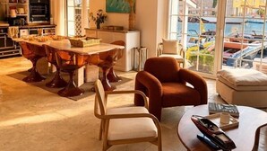 Un vaste espace de vie comprenant une salle à manger, des sièges confortables et de grandes fenêtres donnant sur un port de plaisance.
