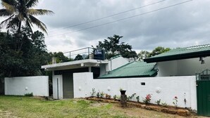A modern house with a green roof, white walls, and a small garden with flowers and a palm tree. - Room-charming 3-bedroom Apartment With G (Kandy)