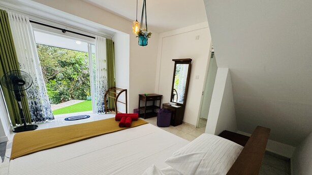 A bedroom with a bed, a wooden bench, a small table, a mirror, and a view of greenery outside. - Room-charming 3-bedroom Apartment With G (Kandy)