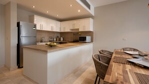 Een moderne keuken met witte kasten, roestvrijstalen apparatuur en een houten eettafel met stoelen.