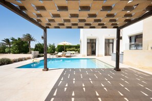 A modern outdoor pool area with a pergola, lounge chairs, and a clear view of the pool. - Vesta - Luxury Villa - 4BR - Cyan (El Gouna)
