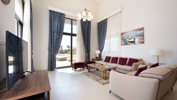 Ein modernes Wohnzimmer mit einem Flachbildfernseher, einem Holztisch, einem beige farbenen Sofa und einem roten Sessel.