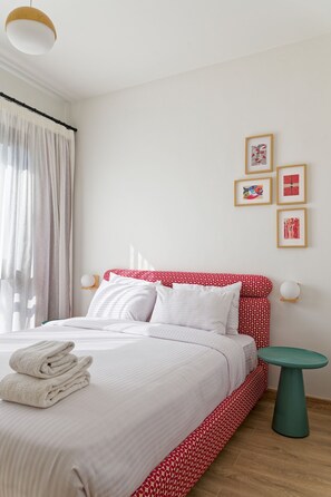A neatly made bed with white and red bedding, a small round table, and wall-mounted light fixtures. - Vesta - Luxury APT - 2BR - Kamaran (El Gouna)