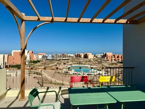 A balcony with a view of a pool and buildings in the background. - Vesta - Luxury APT - 2BR - Kamaran (El Gouna)