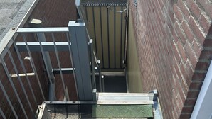 Uma escadaria externa estreita que leva a um portão, cercada por muros de tijolos e um portão de metal.