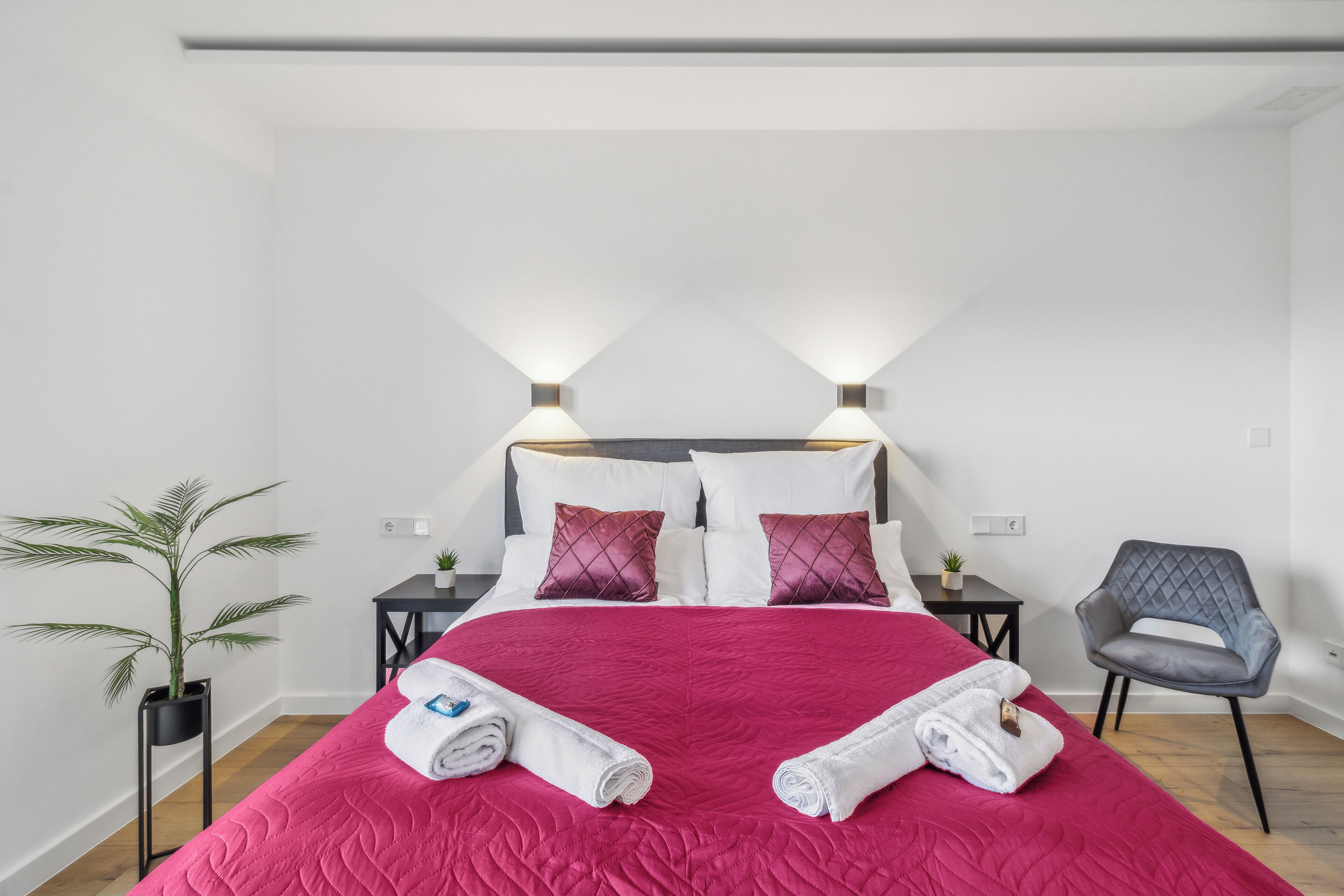 A hotel room with a large bed, two bedside tables, a potted plant, and a chair.