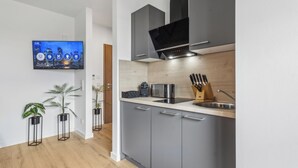 A modern kitchen with grey cabinets, a stainless steel sink, and a flat-screen TV mounted on the wall.