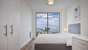 A modern bedroom with a large window, a bed, a bedside table, and a city view. - Quayside Penthouse w/ City Views & Fast WiFi (Greater Manchester)