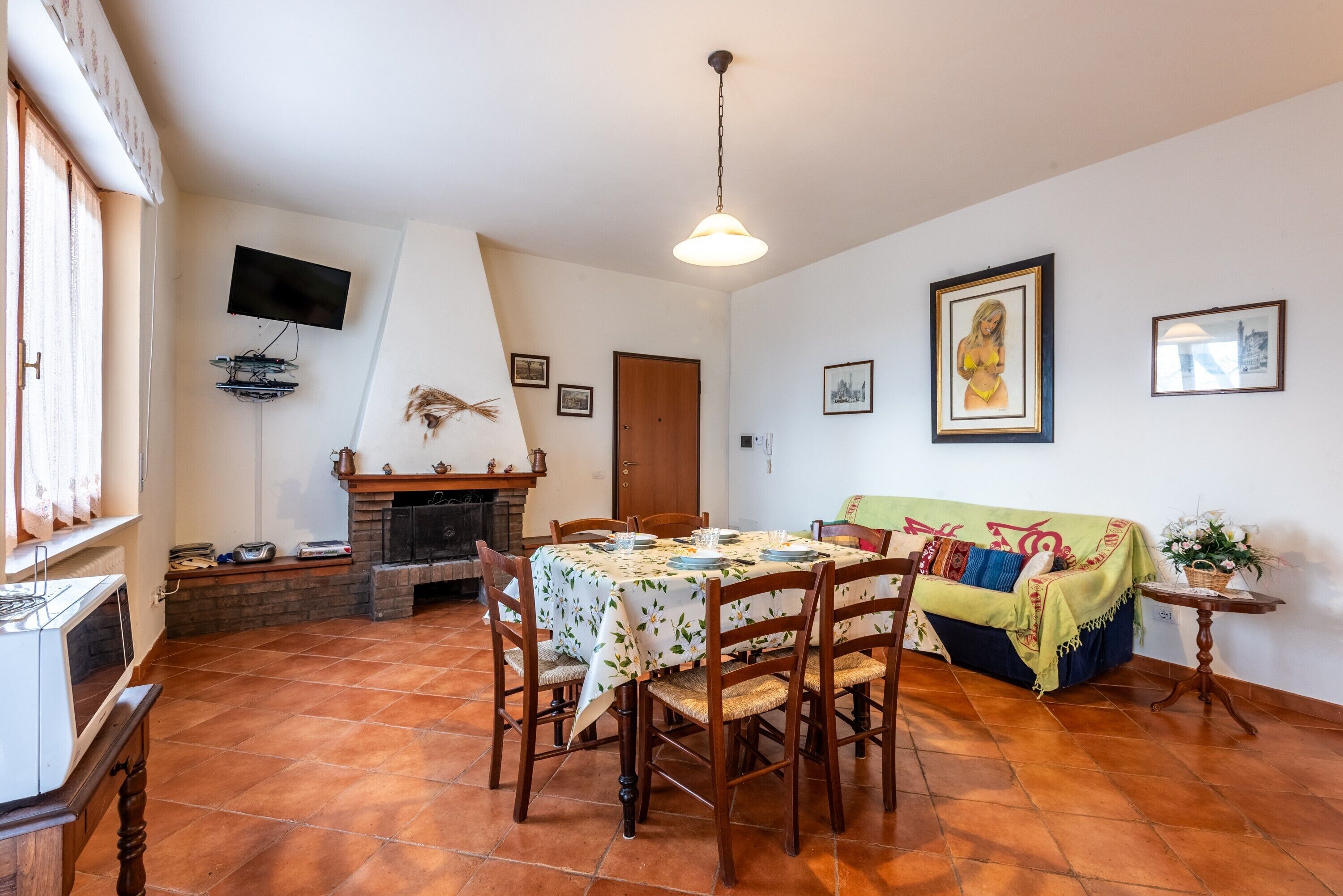 Un comedor con una mesa dispuesta para cuatro, una chimenea, un televisor montado en la pared y un sofá con una manta de colores.