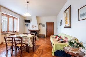 A dining area with a table set for four, a fireplace, and a sofa with a floral arrangement.