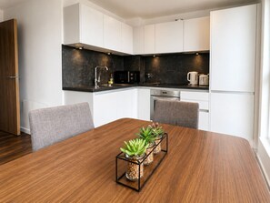 Una cocina moderna con armarios blancos, una encimera oscura y una mesa de comedor con sillas.