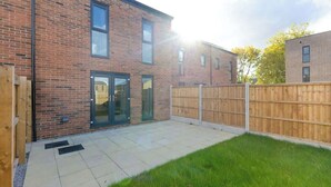 A brick building with a patio area, a wooden fence, and a grassy lawn. - Family-Friendly House Near Manchester, Pet (Greater Manchester)