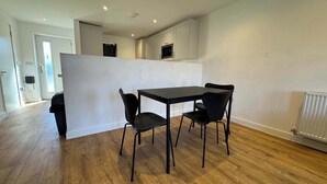 A modern kitchen with a dining area, wooden flooring, and white walls. - Family-Friendly House Near Manchester, Pet (Greater Manchester)