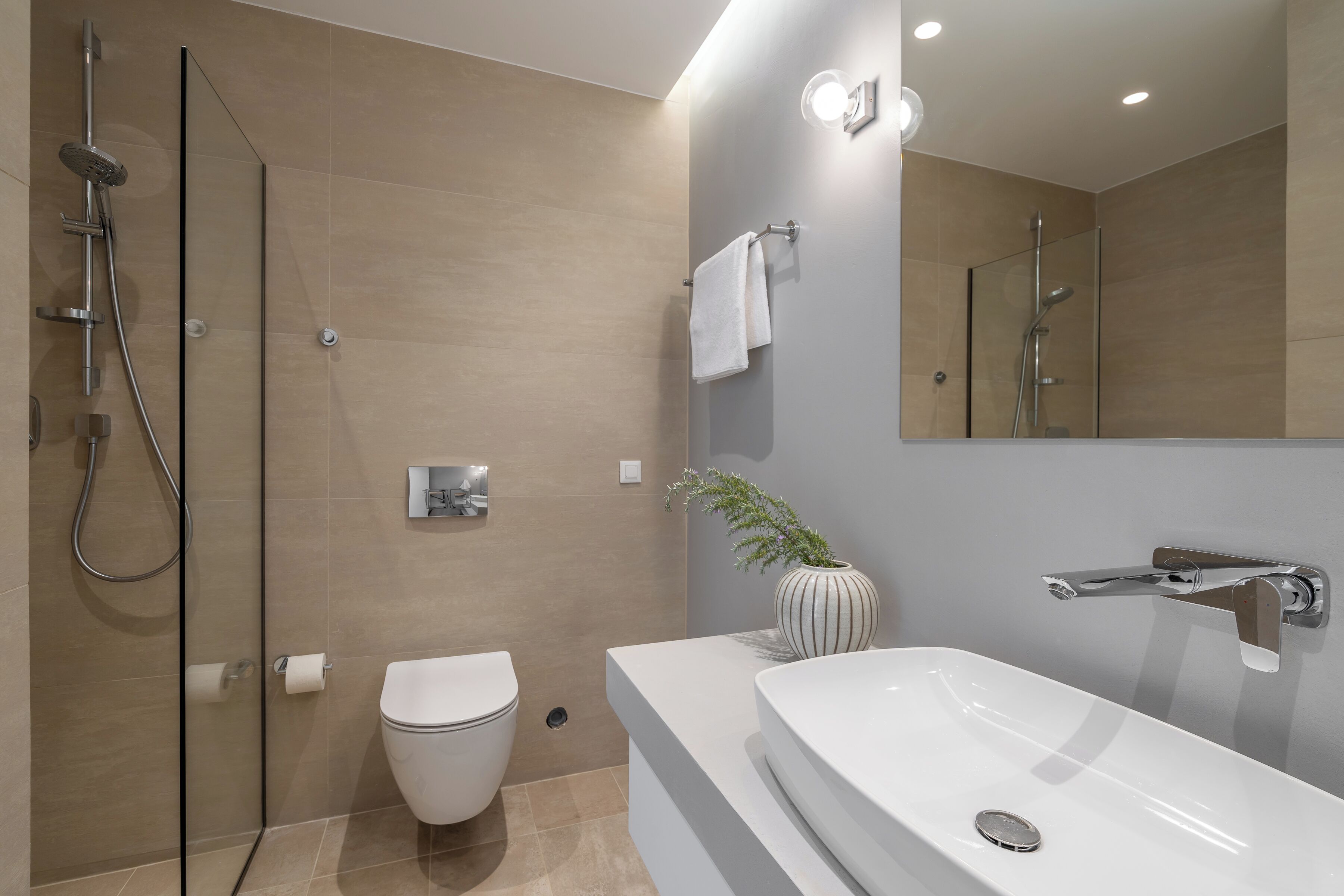 A modern bathroom with a glass shower enclosure, a white toilet, a large bathtub, and a wall-mounted sink.