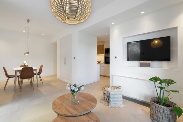 Una sala de estar moderna con comedor, un televisor de pantalla plana en la pared y una planta grande en maceta.