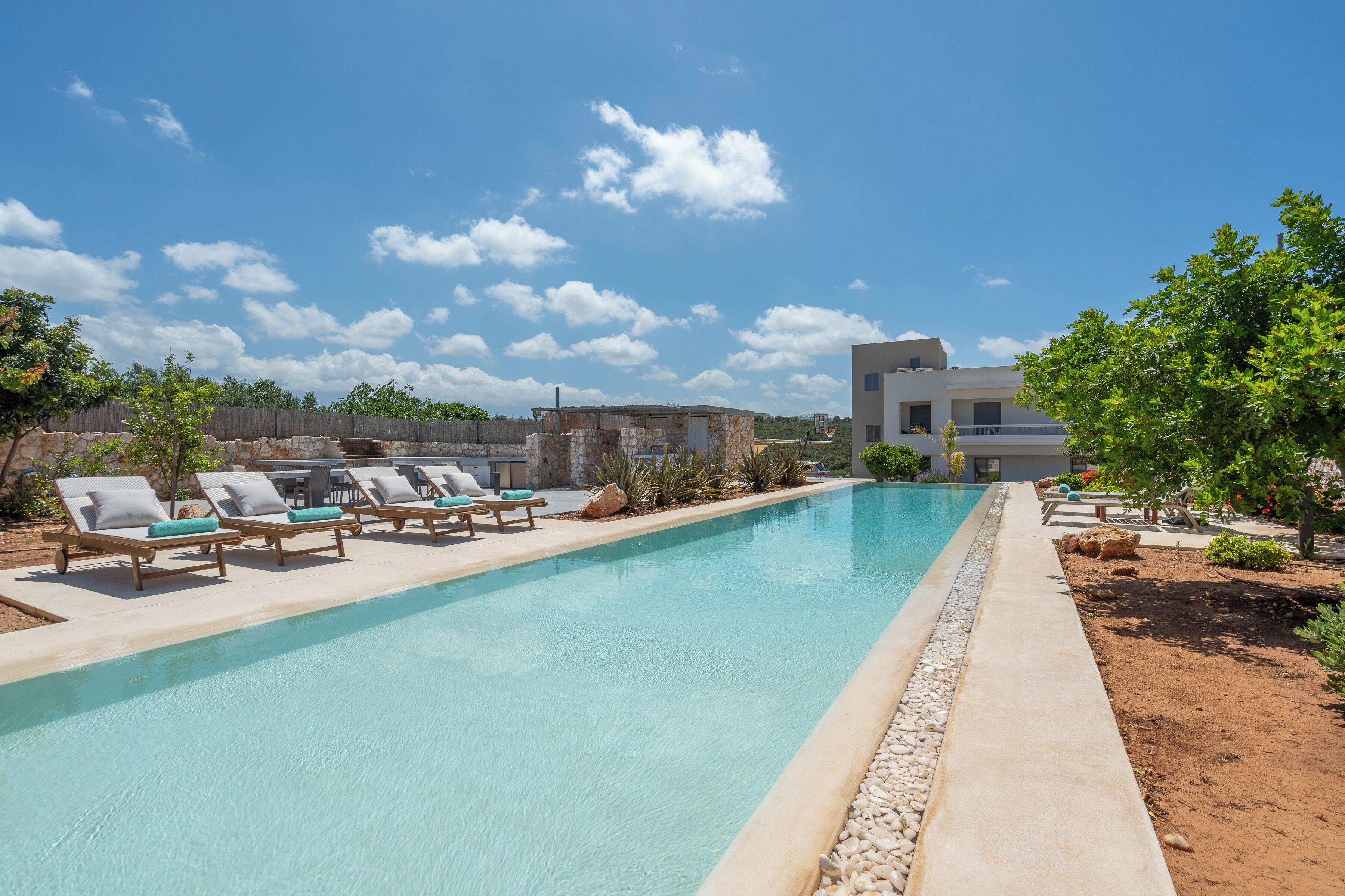 A swimming pool with lounge chairs, a small building, and a modern house in the background.