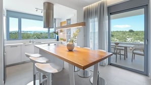 A modern kitchen with a wooden island, white bar stools, and a large window offering a view of greenery. - Le Mont Blanc (Kounoupidiana)