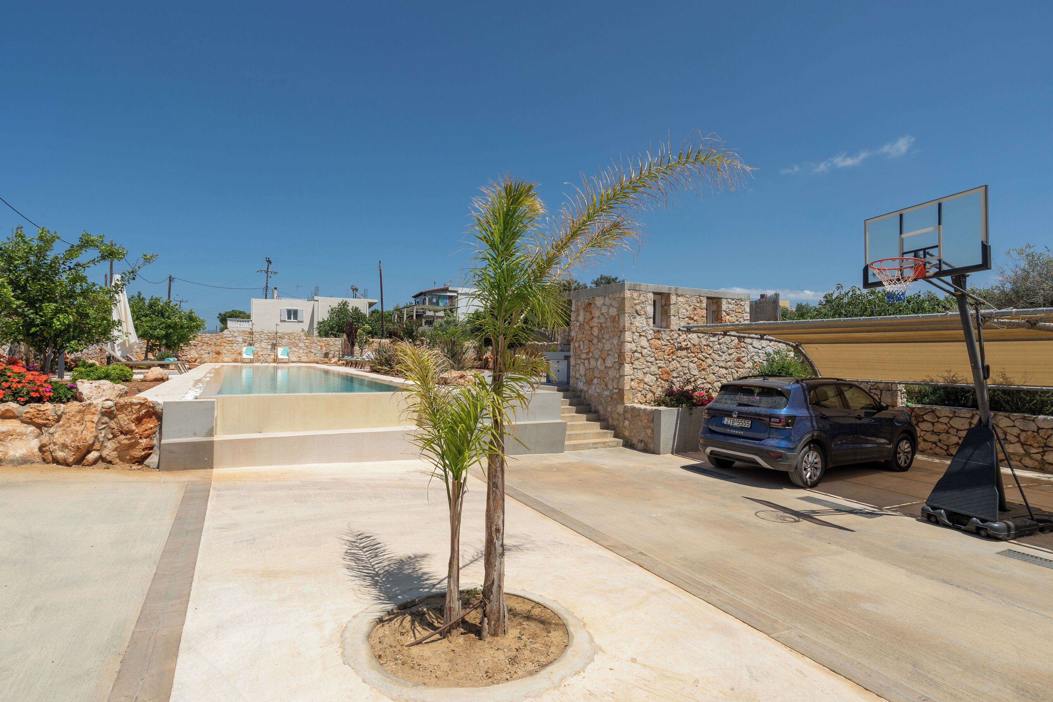 A pool area with a basketball hoop, a stone building, and a parked car.