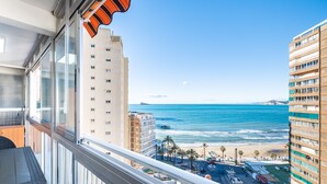 Een balkon met uitzicht op het strand en de oceaan, een hoog gebouw en een heldere lucht.