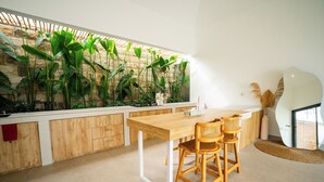 A modern kitchen with a wooden table and chairs, a stone wall with plants, and a large window. - Solla Sol Villa Canggu (Kerobokan)