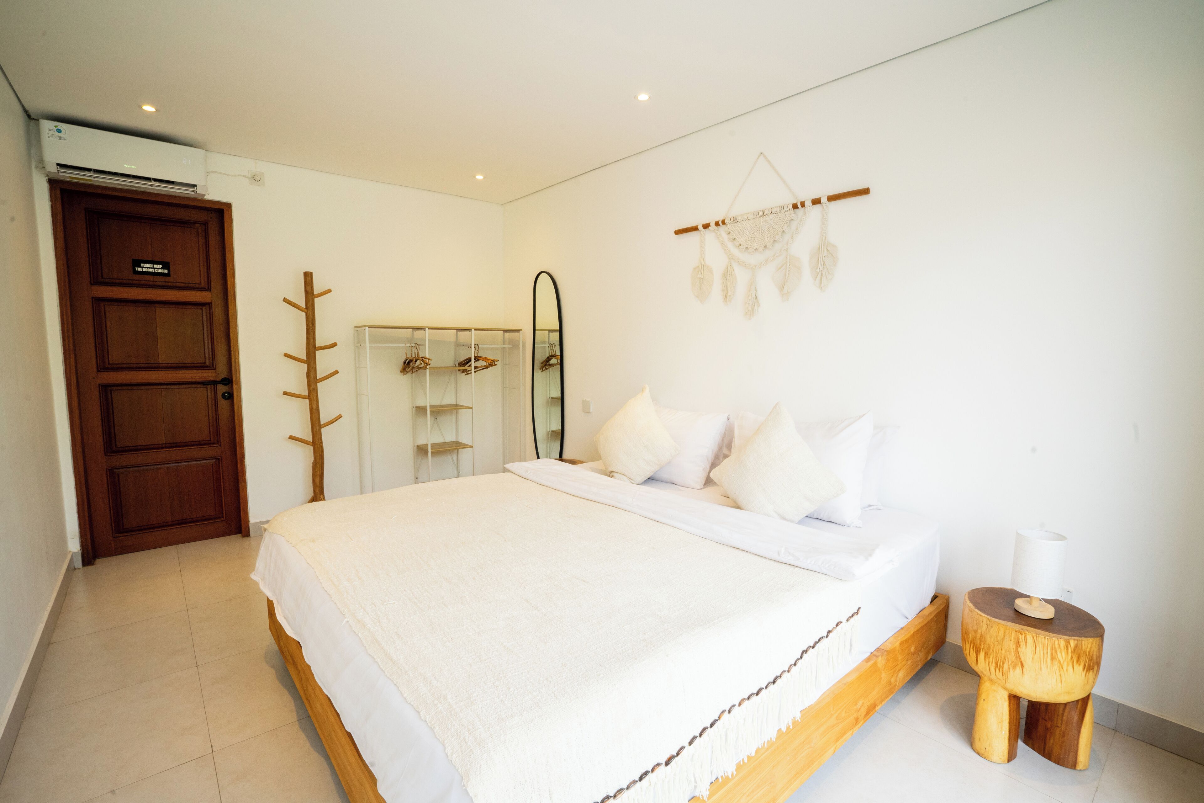 A bedroom with a bed, wooden headboard, bedside table, and a wall-mounted dreamcatcher.