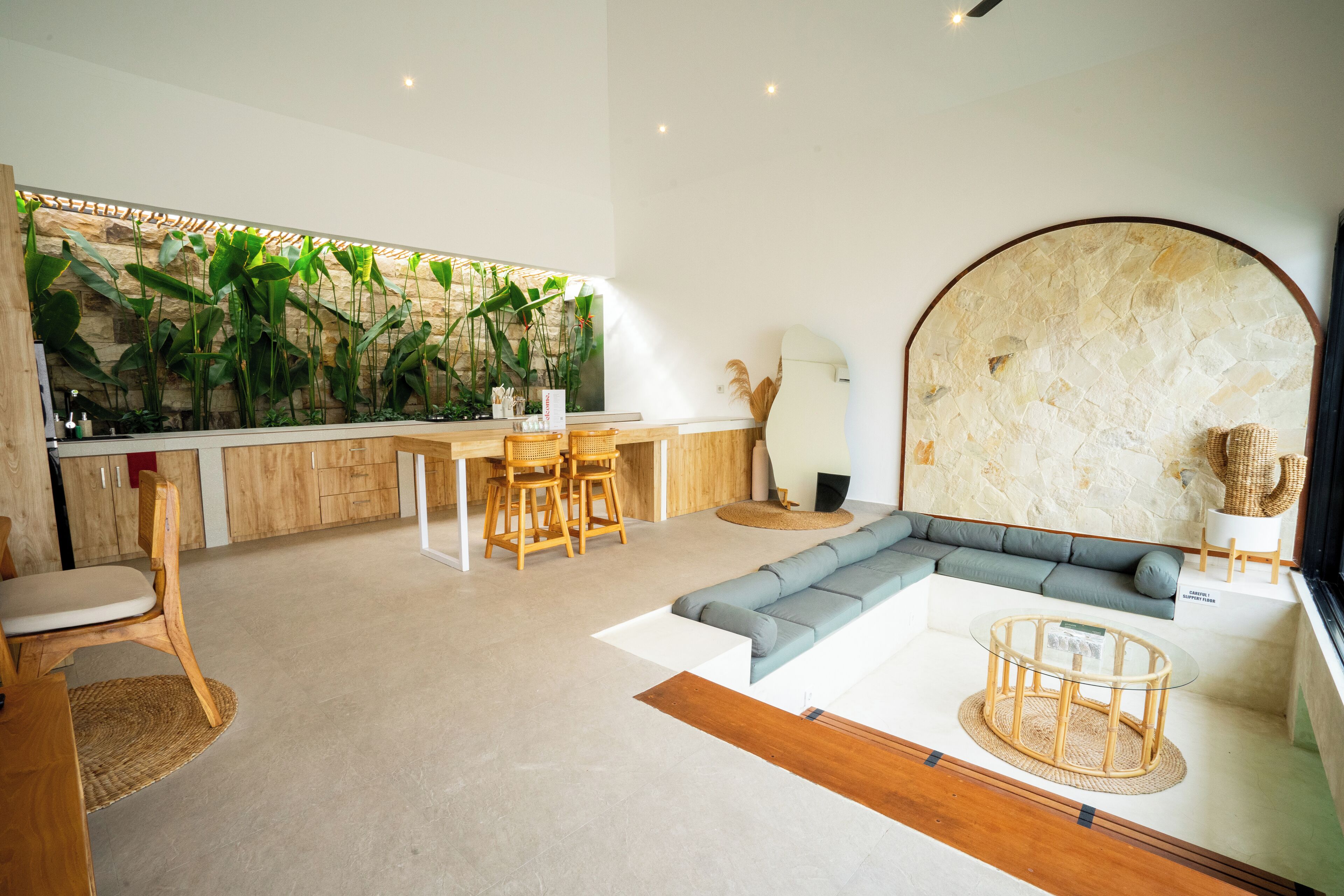 A modern living room with a stone accent wall, a grey sectional sofa, a wooden dining area, and a large plant wall.