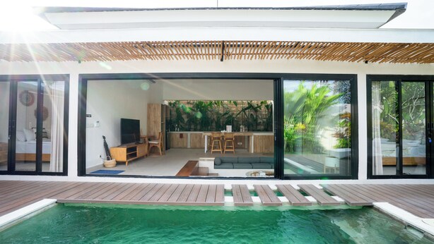 A modern house with a large sliding glass door leading to a living area with a kitchen, a pool, and a wooden deck. - Solla Sol Villa Canggu (Kerobokan)