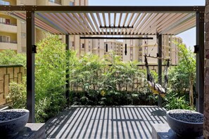 Et overdækket udendørs område med pergola, plantekasser og hængekøje.