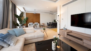 Una sala moderna con un sofá modular, un televisor de pantalla plana y un comedor al fondo.