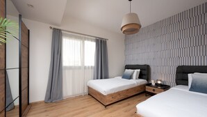 Un dormitorio moderno con dos camas, un ventanal con cortinas translúcidas, una pared a rayas y una lámpara colgante.