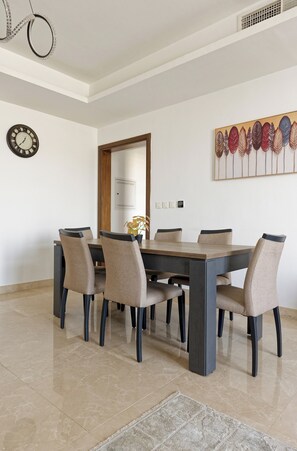 A dining area with a rectangular table, six chairs, a clock, a decorative wall piece, and a door in the background. - Vesta - Luxury Apt- 3BR - Cfc Xli (New Cairo)